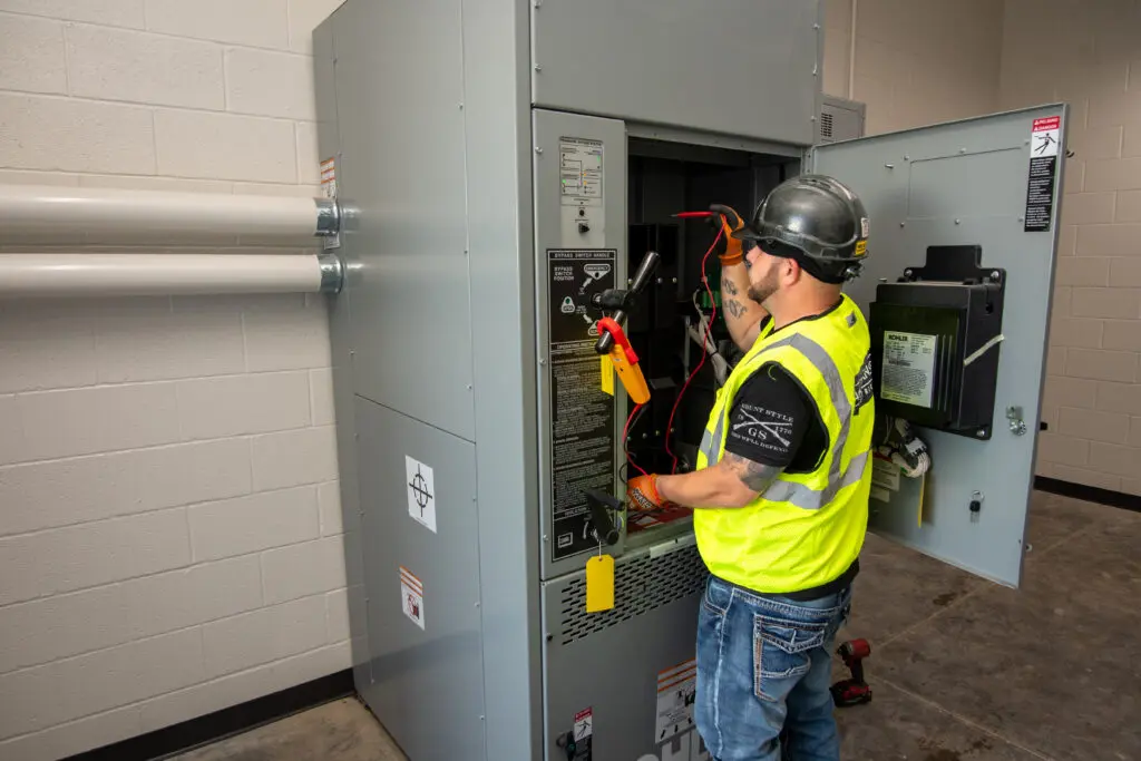 Electrician in hi-vis vest working on large electrical panel