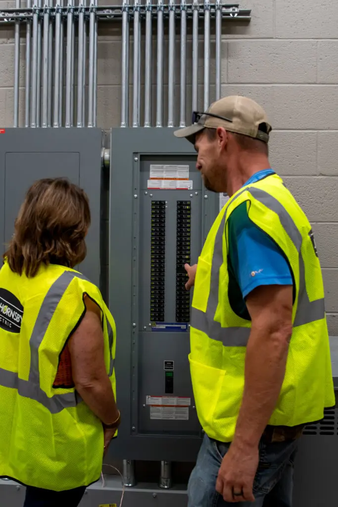 Two electricians in hi-vis vest working on large electrical panel box