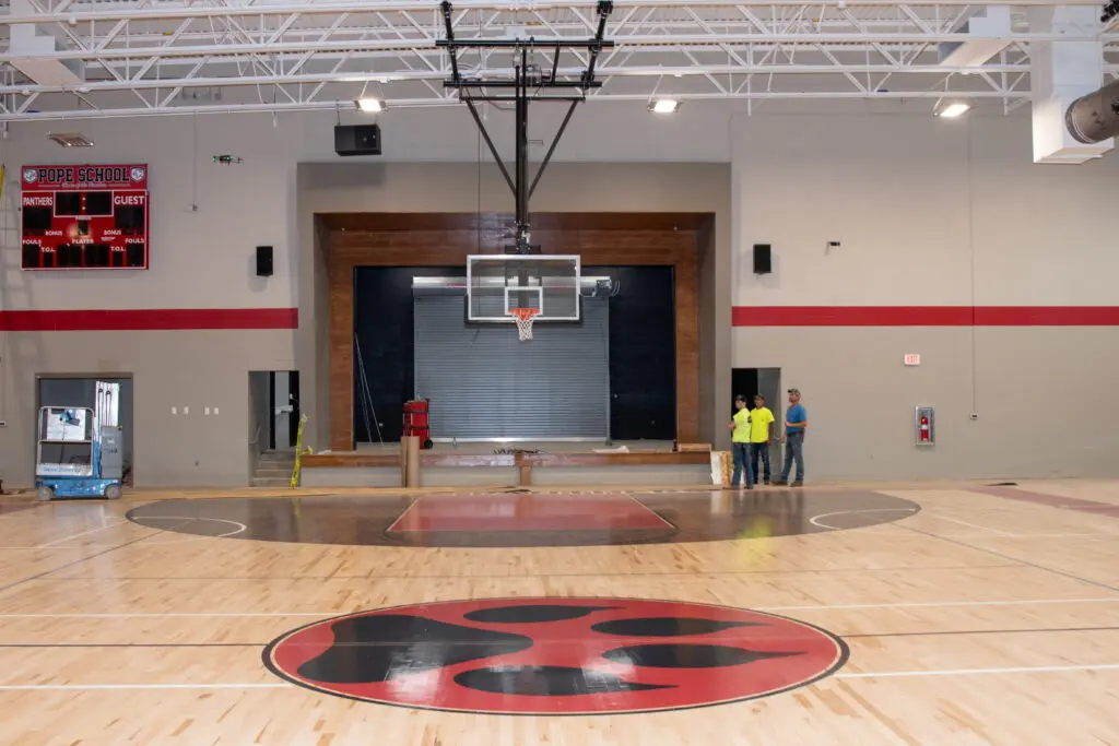 Three electricians in the background by a door in a wide view of the Pope Elementary School gym in Jackson Tennessee